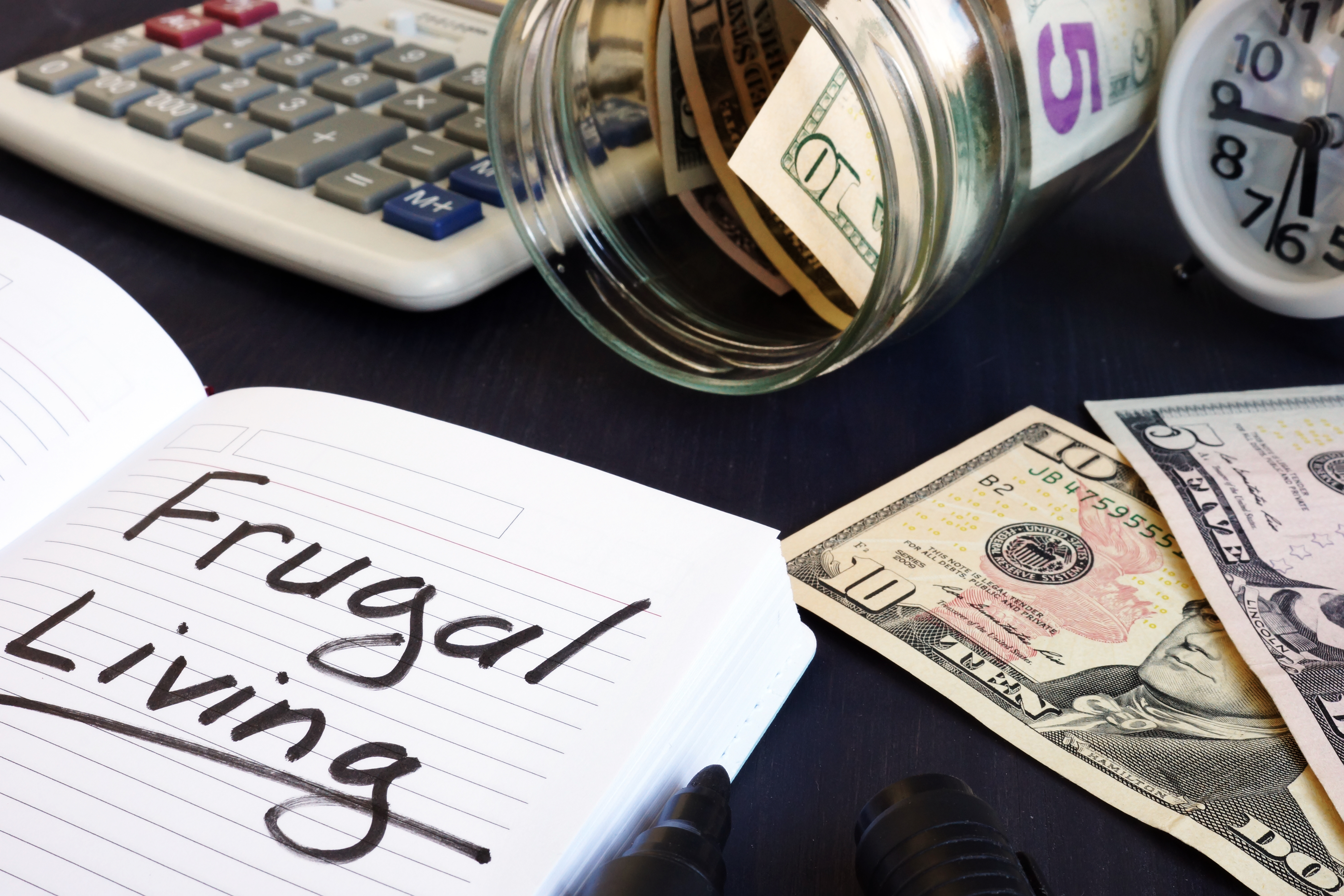 Frugal living written in notebook on table with cash and calculator