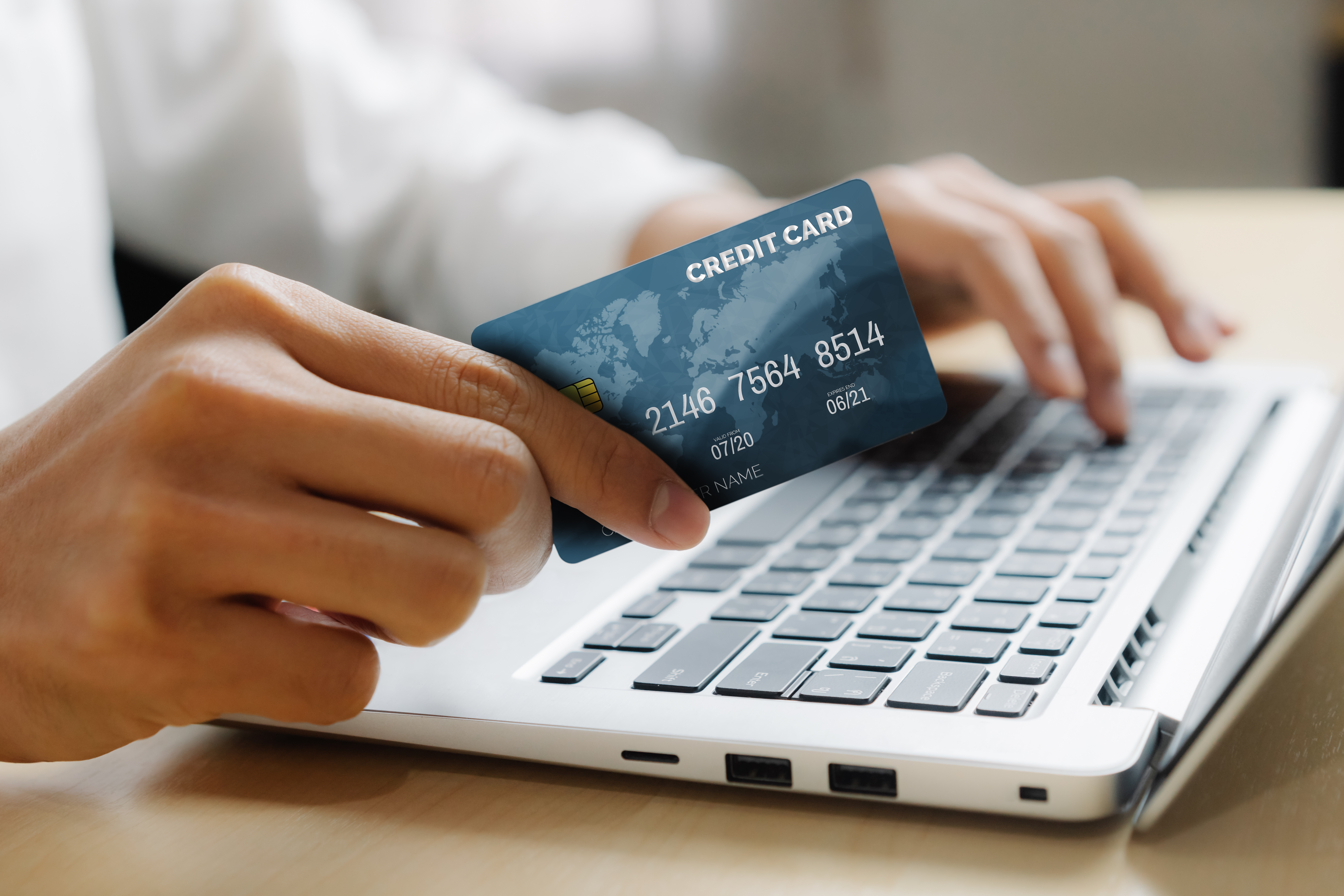 person holding credit card in hand while typing with other on laptop