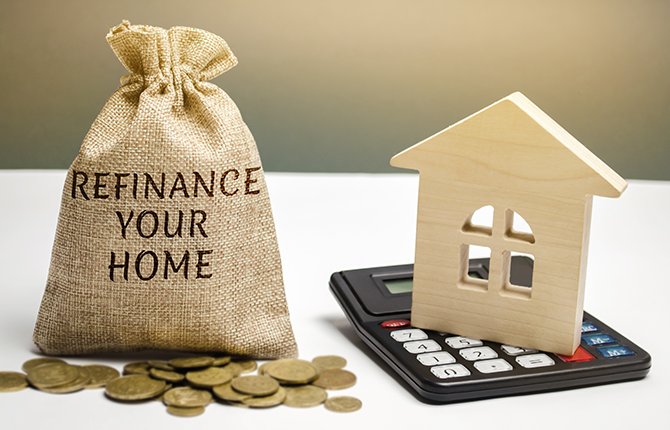 bag of coins labeled refinance your home with wooded play house and calculator on table