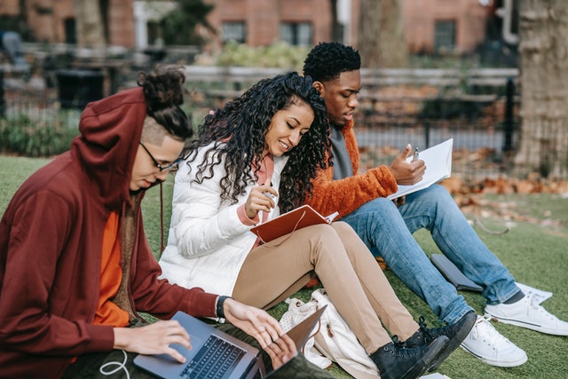 Three college students sitting on grass studying