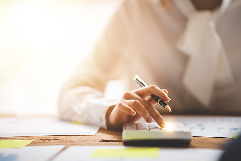 Person sitting at table holding pen using calculator