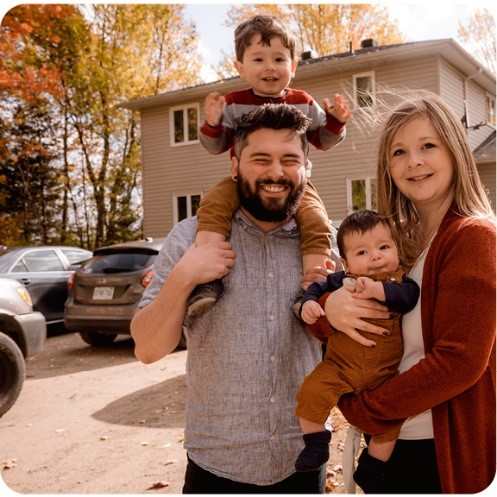 Smiling man and woman standing in front of home holing babies.