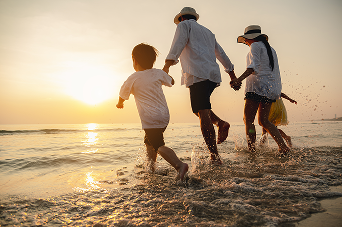 family of four running through water on sunset beach