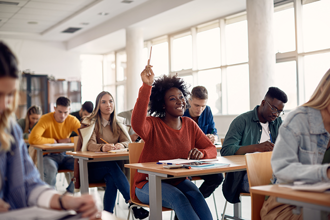 Happy student raising arm to answer question while attending class