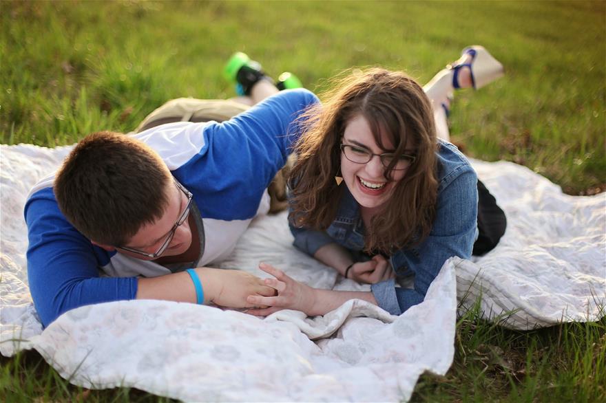 Man and woman laying on blanket in field laughing.