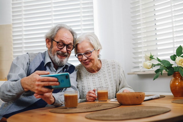 Elderly man and woman sitting at table drinking coffee looking at mobile phone.