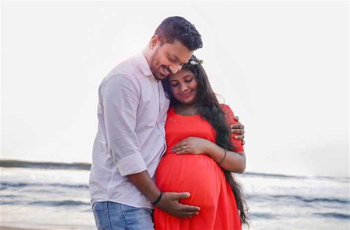 Man embracing pregnant wife on beach.