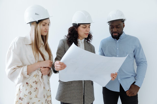 Three contractors in hardhats reviewing a blueprint