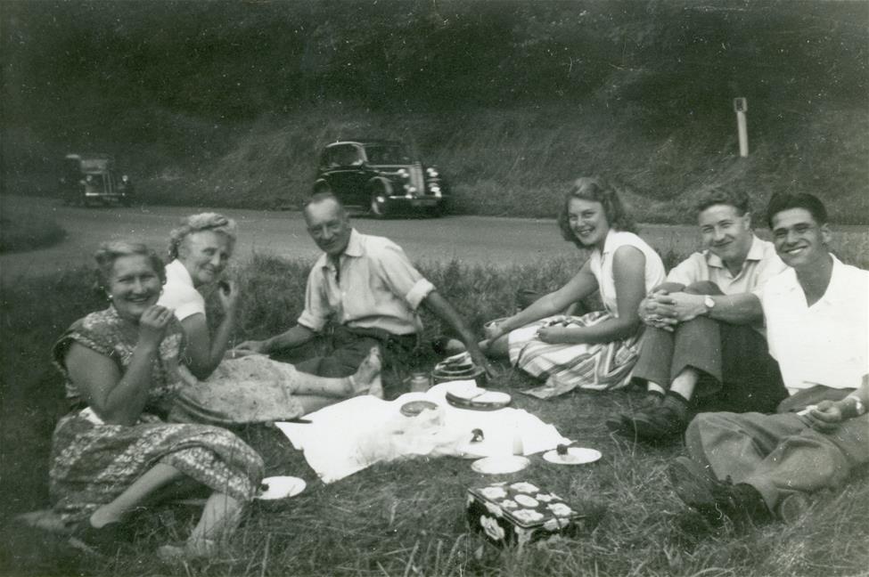 black and white image of group of men and women having a roadside picnic in 1950s