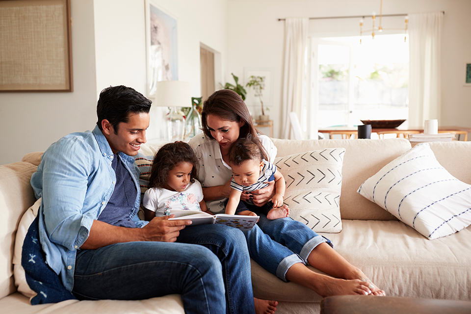 Family of four sitting on a couch reading a book.