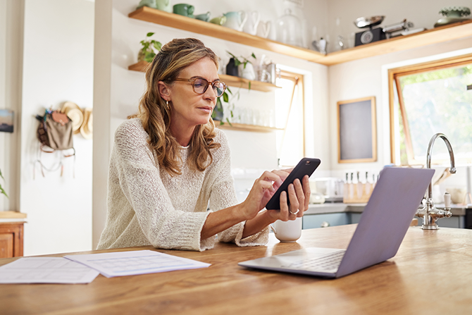 woman sitting at dining room table working on phone and laptop
