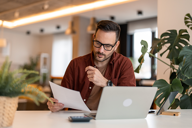 Serious millennial man using laptop sitting at the table in a home office