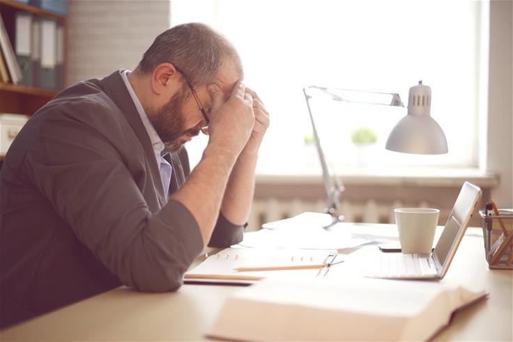 Frustrated man sitting at a desk with his head in his hands.