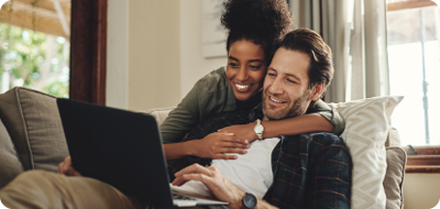 Smiling man sitting on couch working on laptop and smiling woman hugging him from behind