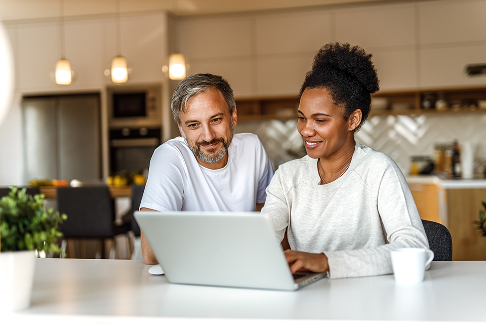 happy couple siting at kitchen table working on laptop.