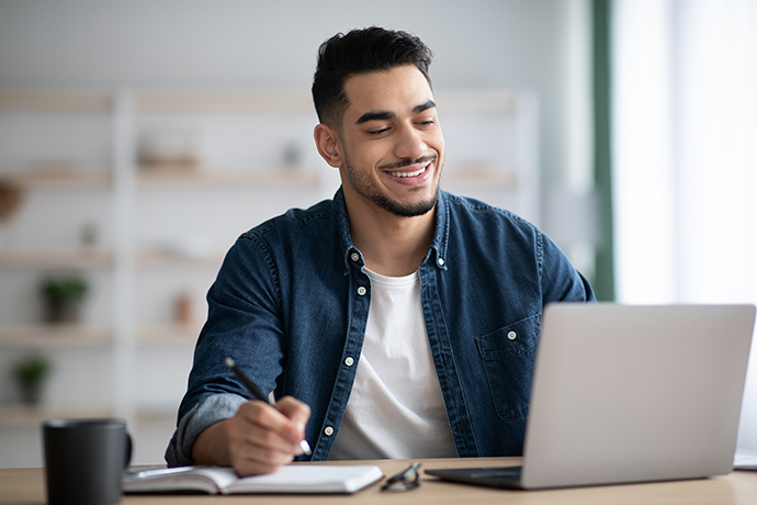 Cheerful guy working on laptop, taking notes
