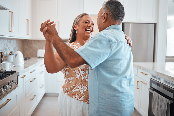 Elderly man and woman with smile dancing together in kitchen