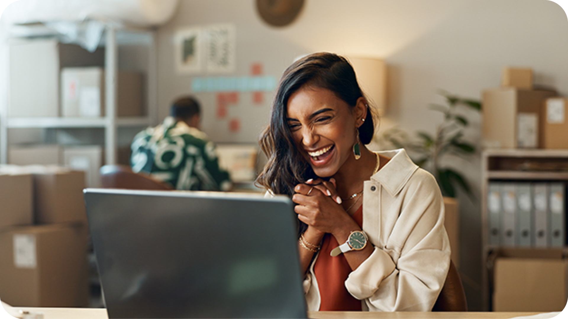 excited smiling woman sitting at desk clasping hands together working on computer