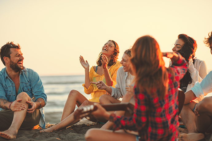 group of friends sitting on beach laughing together