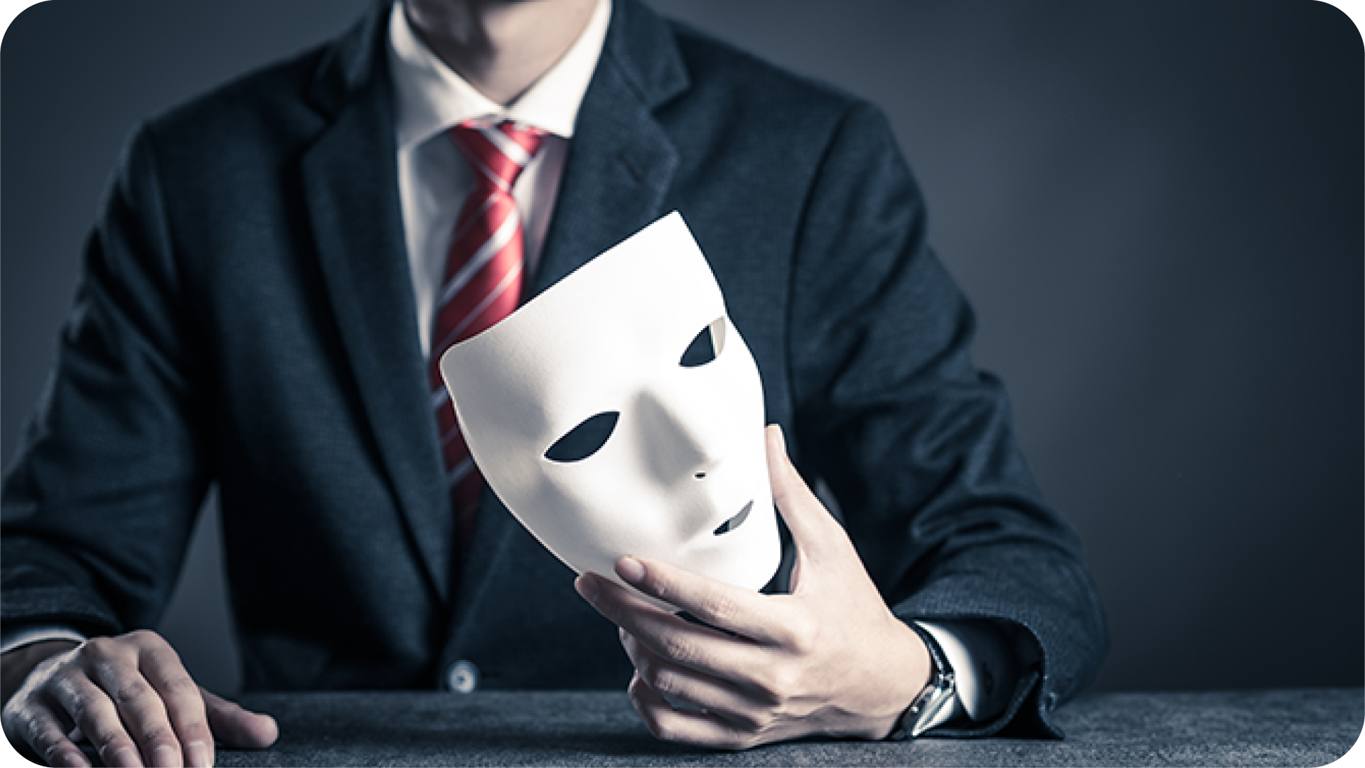 man in suit sitting holding white mask in had hiding identity