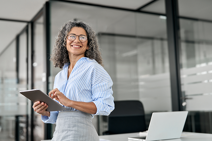 mature professional business woman holding digital tablet pad standing in office at work