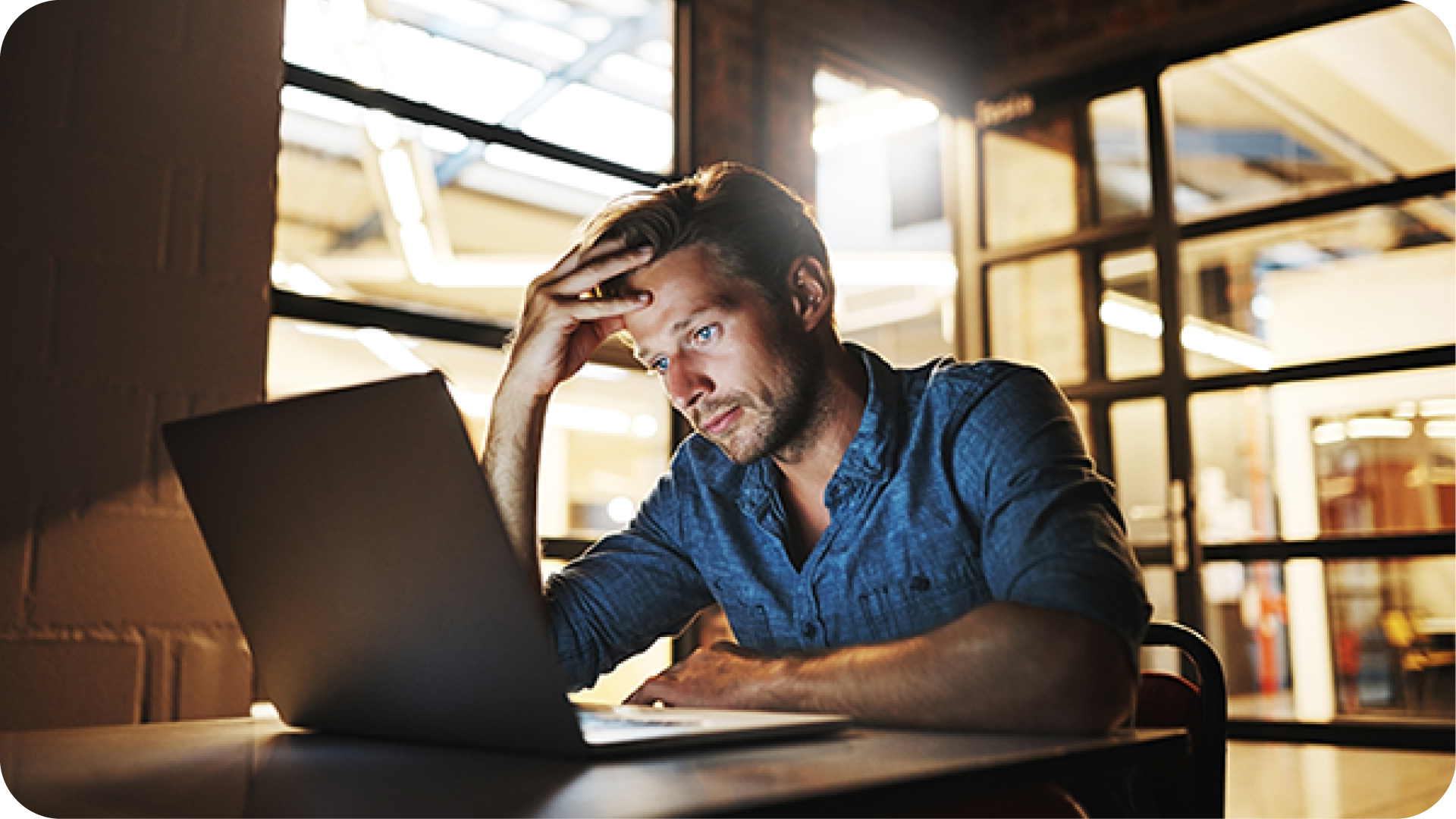 pensive man sitting at desk staring at computer on desk with head in hands