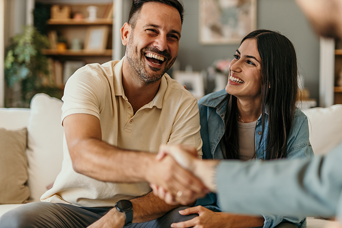 The young happy couple and an agent shaking hands in a new property