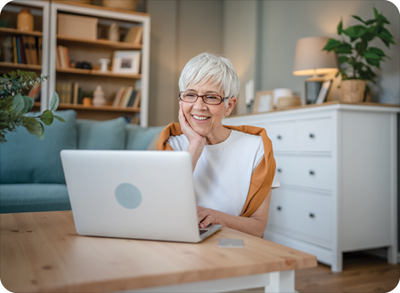 white haired woman sitting at coffee table smiling at laptop