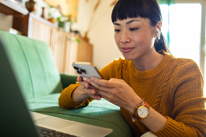 woman using smartphone in front of laptop on couch at home