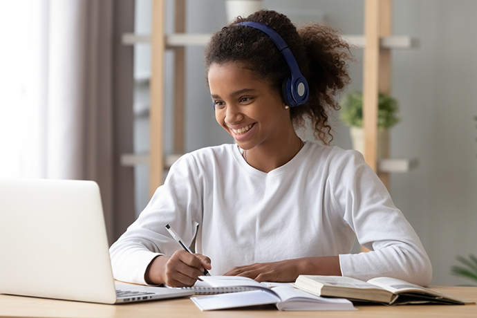 Young teenage girl listening to music on headphones and working on laptop