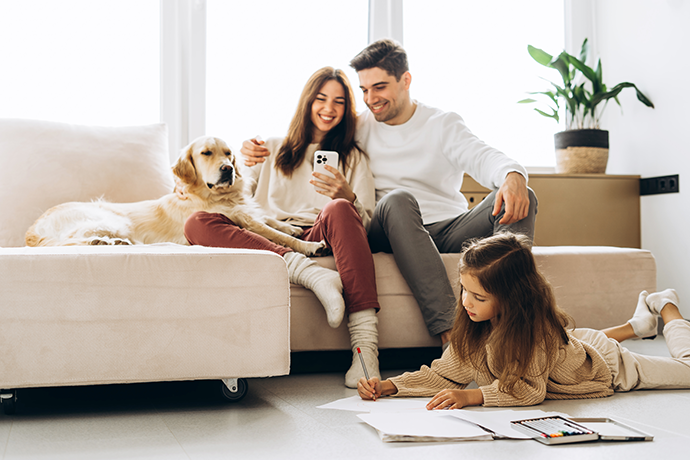 Family enjoying time together at home, parents using smartphone and daughter drawing