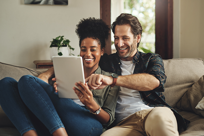 Happy couple relaxing on couch working on tablet
