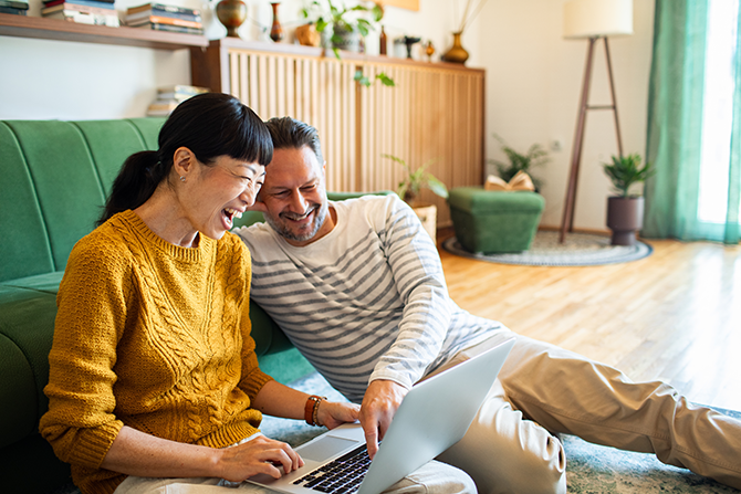happy couple sitting on floor in livingroom working on laptop