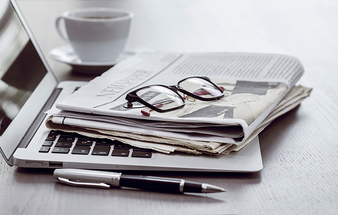 newspaper laying on laptop with glasses on top