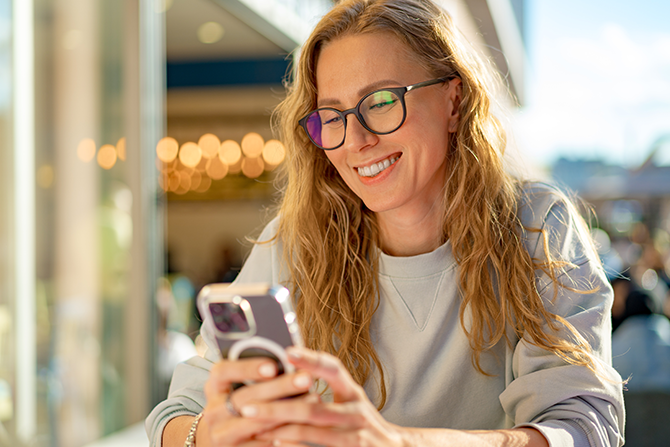 Young woman smiling at phone outside at a cafe