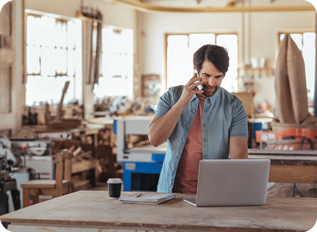 Woodworker using a phone and laptop in his large workshop Woodworker using a phone and laptop in his large workshop