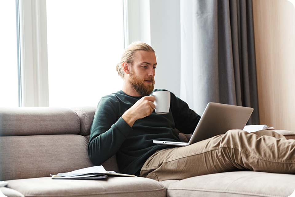 Concentrated young bearded man sitting in home using laptop computer Concentrated young bearded man sitting in home using laptop computer